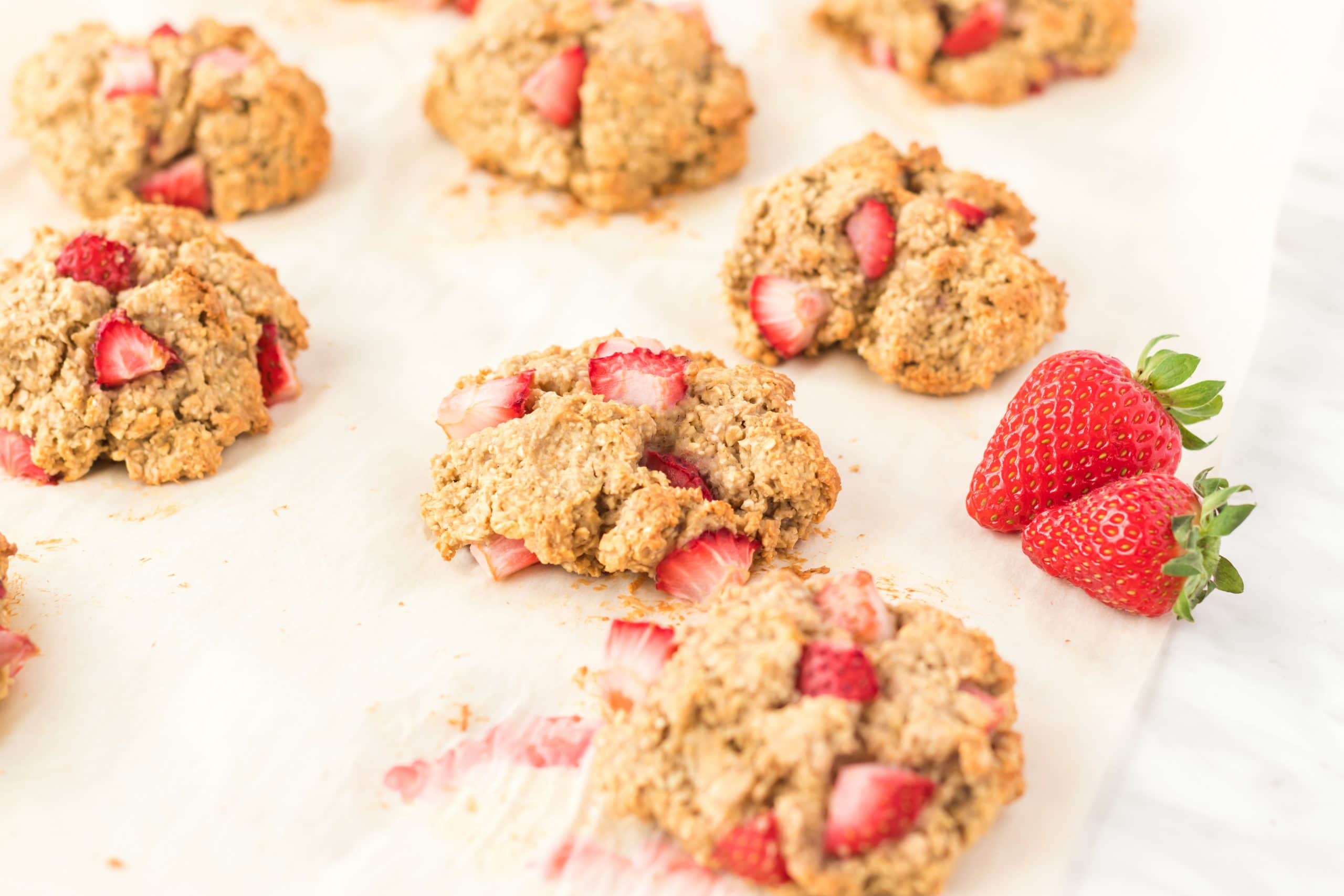 berry scuffins spread out on parchment paper with fresh strawberries
