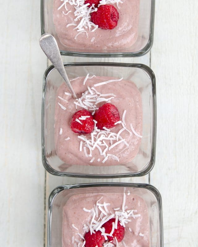 A light, fresh, vegan raspberry pudding, shown served in individual dishes topped with shredded coconut and fresh raspberies.