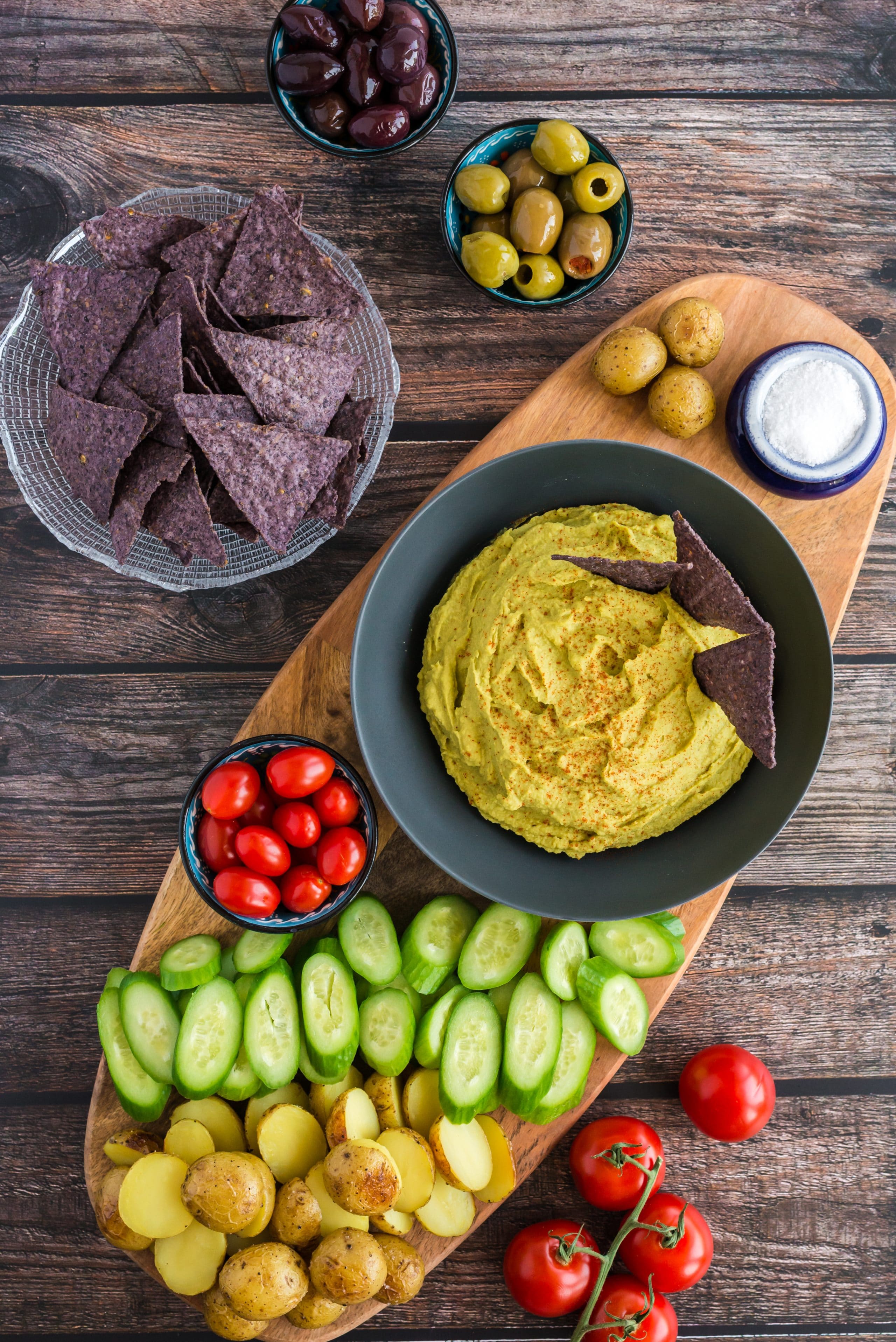 Green Pea Hummus on cutting board surrounded by fresh vegetables and tortilla chips