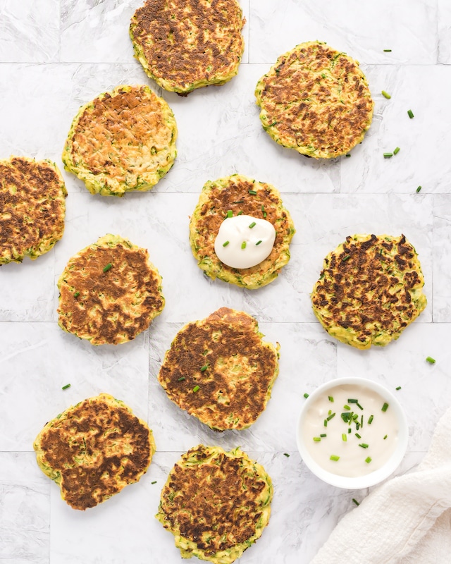 overhead photo of zucchini fritters on countertop with dip