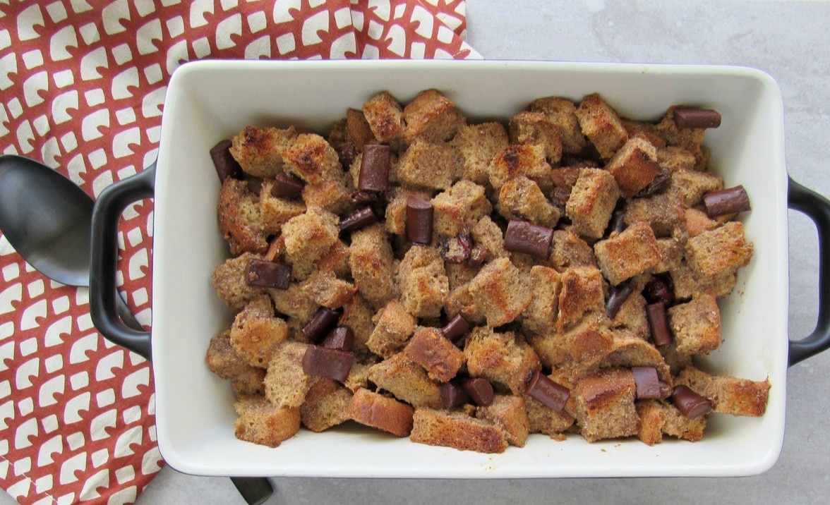 Vegan Bread Pudding with Chocolate Pieces. Bread Pudding is shown in baking dish with serving spoon at the side.