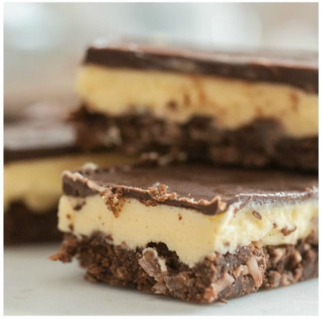 A favorite for vegan easter desserts: Dreena's popular Vegan Nanaimo Bars! Shown sliced and stacked, with one large in forefront of photo.